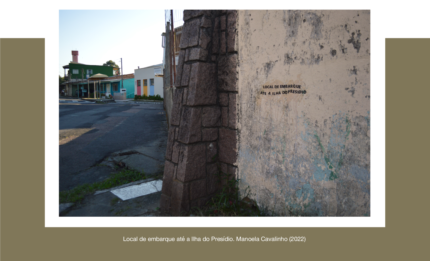Fotografia colorida. Retrata parte de um muro, onde foi adesivada a seguinte frase: Local de embarque até a Ilha do Presídio